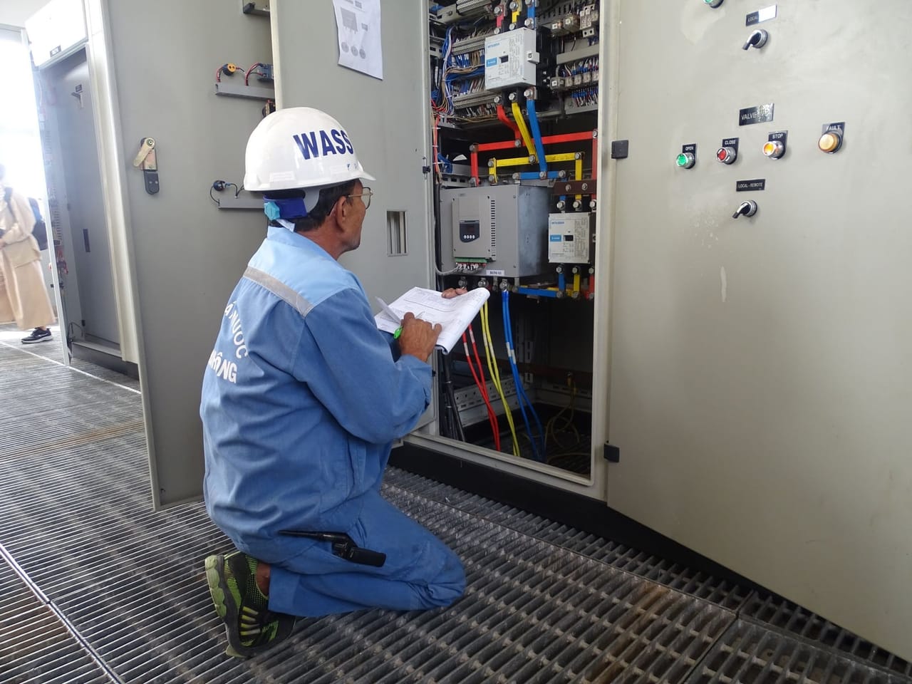 Technician in a hard hat inspecting an open electrical panel